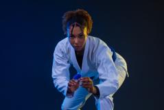 Atleta de jiu-jítsu em ação, utilizando um quimono branco, demonstrando técnica e foco em um ambiente de treino com fundo escuro e azul.