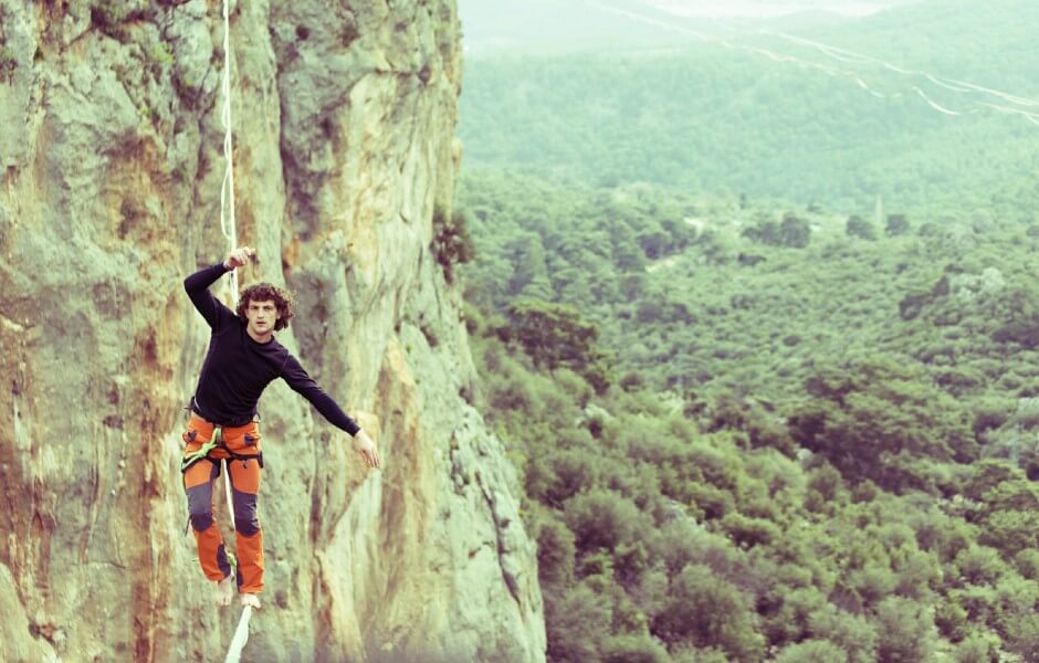 Imagem de um praticante de slackline se equilibrando em uma corda esticada entre duas montanhas.