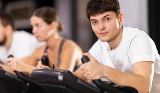 Três jovens fazendo exercício em bicicletas ergométricas em uma academia.