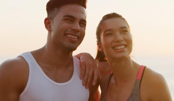 Casal sorridente ao ar livre, aproveitando um momento juntos em um cenário ensolarado, refletindo felicidade e companheirismo.